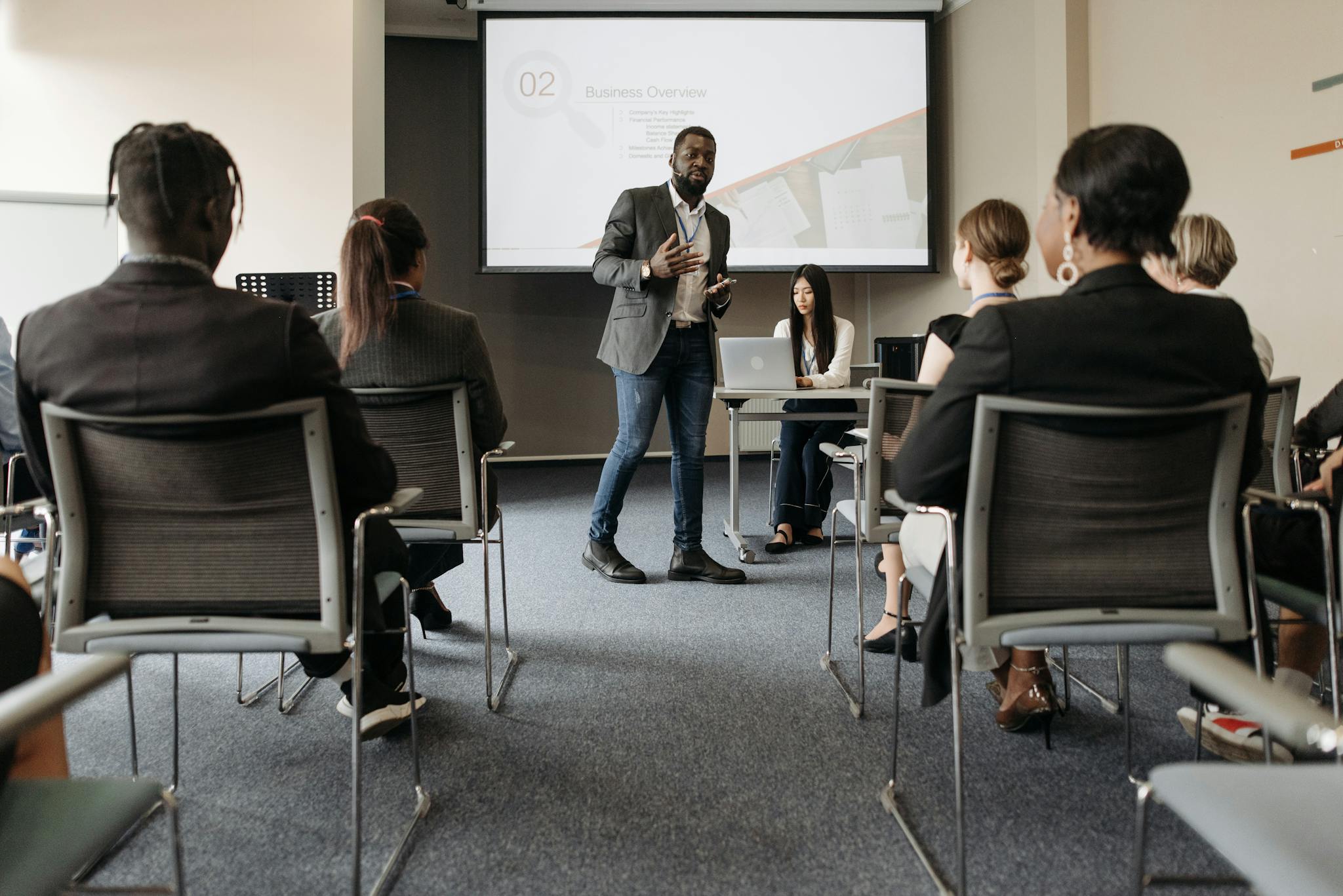 Diverse group attending a business seminar with a presenter and screen display.